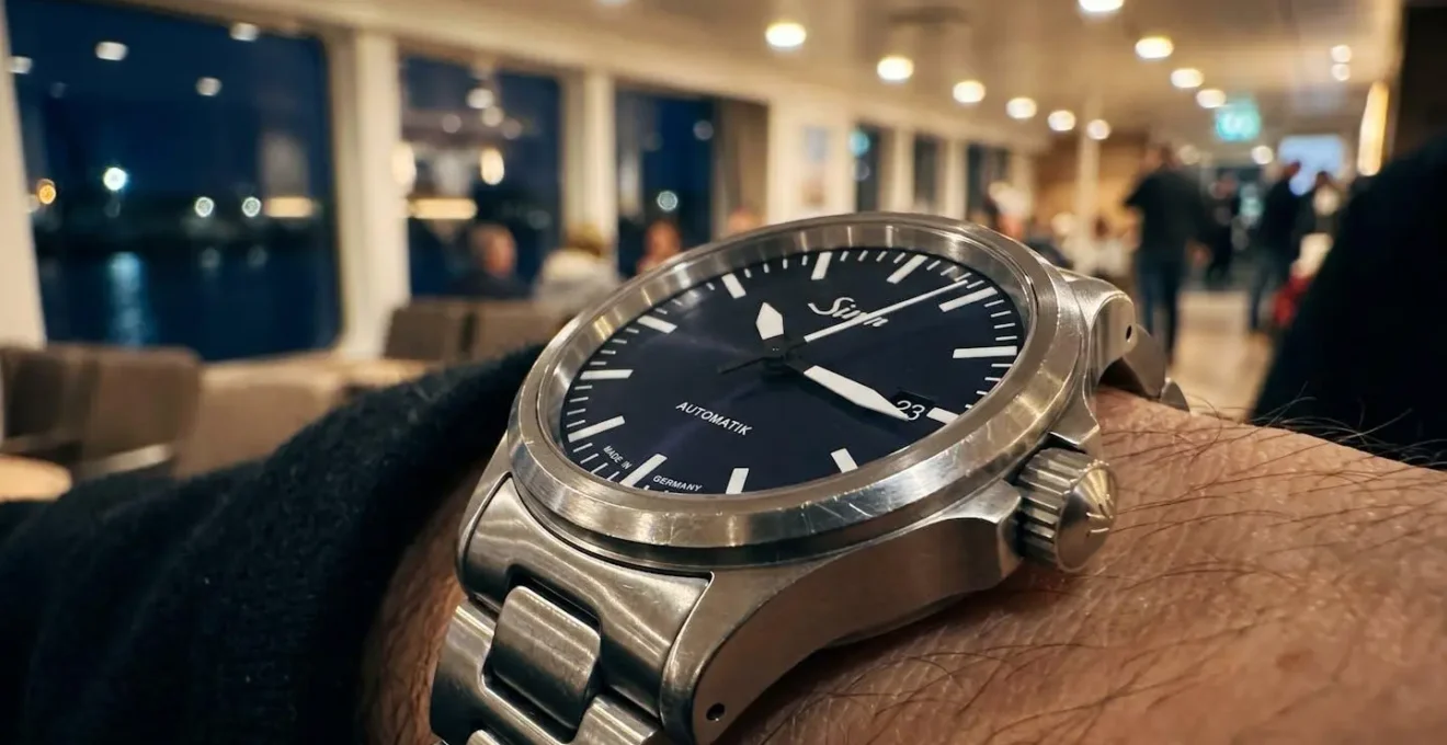 Extreme Nahaufnahme einer Armbanduhr, die 23 Uhr zeigt, mit unscharfem Bokeh-Hintergrund eines modernen Fährinnenraums